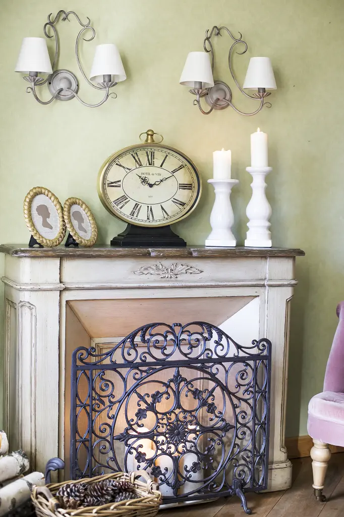 фальш-камин со свечами, закрытый чугунной решеткой, с часами на столешнице и двумя бра над ним.jpg
