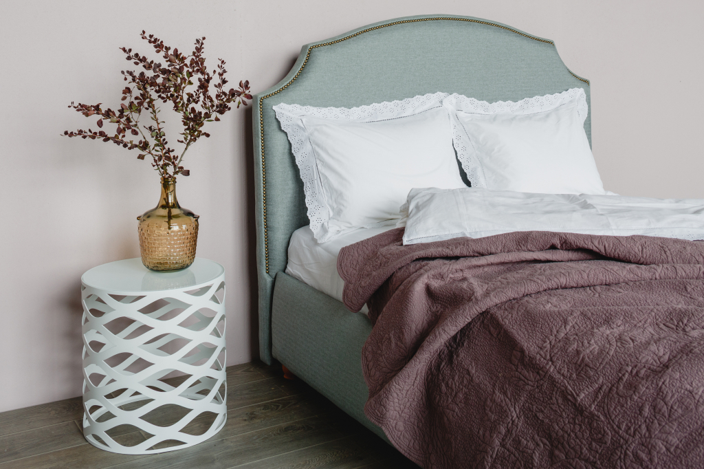 мягкая кровать цвета шалфея с отделкой декоративными гвоздиками и стильный белый прикроватный столик.jpg