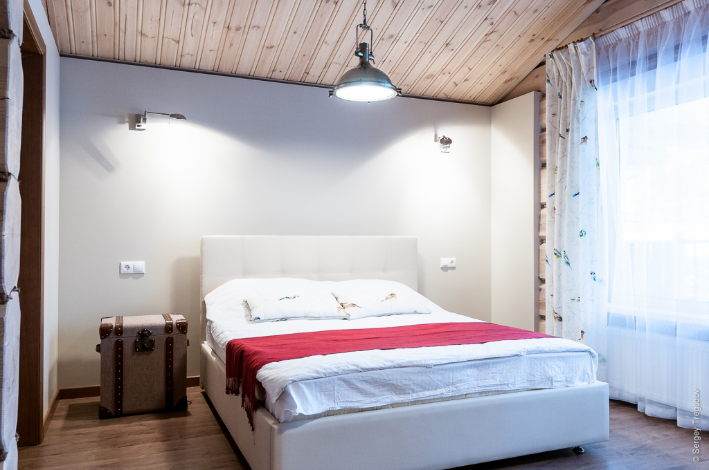 спальня в деревянном доме с белой мягкой кроватью из эко-кожи и сундуком вместо прикроватной тумбочки.jpg