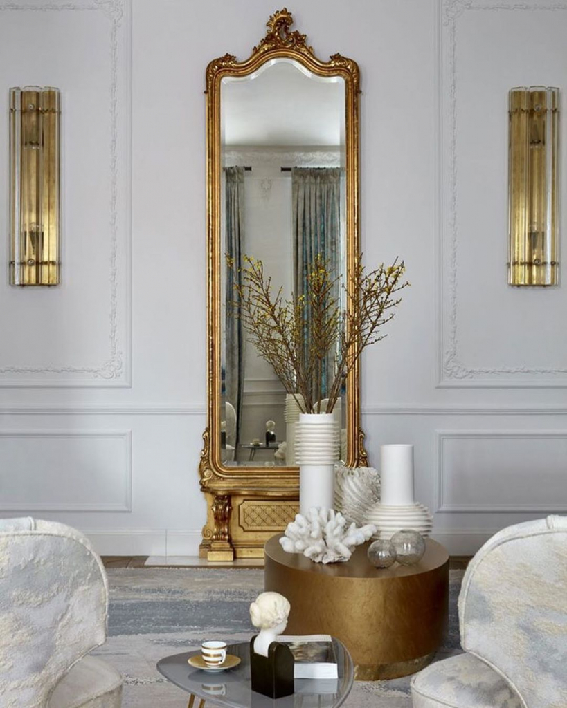 белая гостиная с высоким зеркалом в золотой раме, золотыми светильниками на стенах и золотым журнальным столиком.jpg
