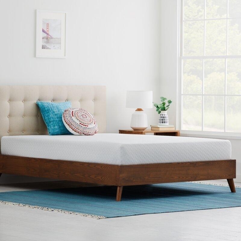 современная светлая спальня с деревянной кроватью, бирюзовым ковриком на полу и бирюзовой декоративной подушкой.jpeg