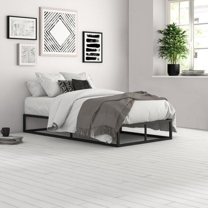 белая спальня в минималистическом стиле с черным металлическим основанием кровати и черно-белыми постерами на стене.jpeg